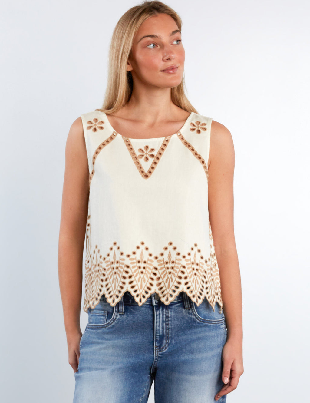 Woman wearing a sleeveless crochet top with floral patterns and blue jeans on a light gray background
